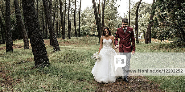 Happy bride and groom walking in forest