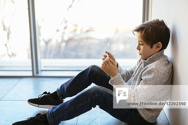 Junge sitzt auf dem Boden und schaut auf sein Handy.