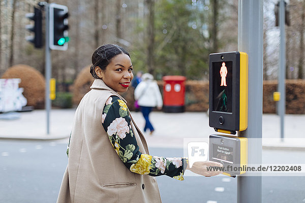 UK  London  Porträt einer lächelnden Frau  die den Knopf des Fußgängerlichts drückt.