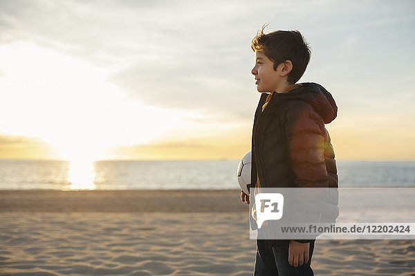 Junge mit Fußball am Strand bei Sonnenuntergang