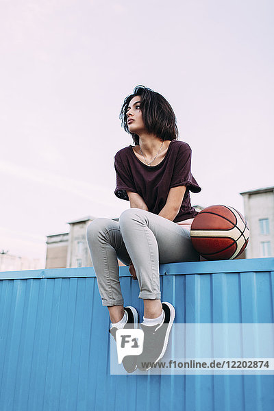 Junge Frau mit Basketball auf Container sitzend