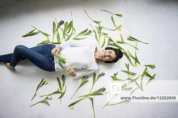 Lächelnde Frau mit Kopfhörer inmitten von Tulpen auf dem Boden liegend