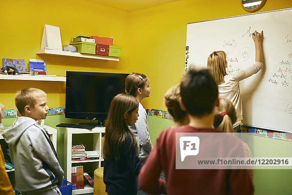 Lehrer mit Schülern  die auf Whiteboard schreiben