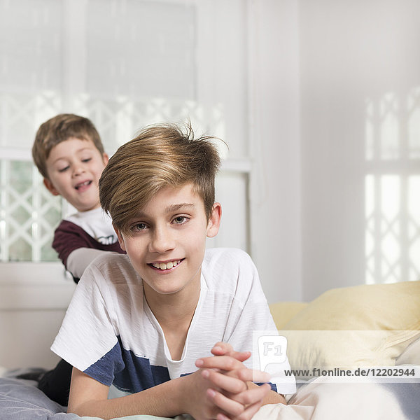 Porträt eines lächelnden Jungen mit einem jüngeren Bruder  der zu Hause auf dem Bett liegt.