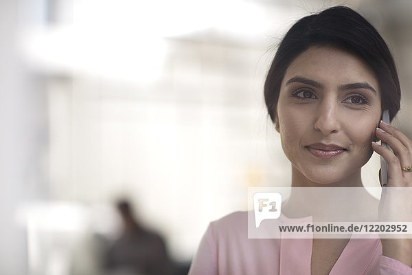 Porträt der lächelnden jungen Frau am Handy im Büro