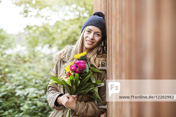 Portrait of smiling young woman holding bunch of flowers outdoors