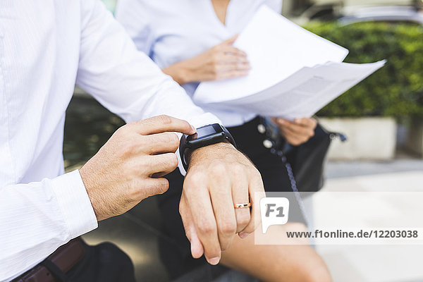 Businessman with smartwatch and businesswoman with documents in the city