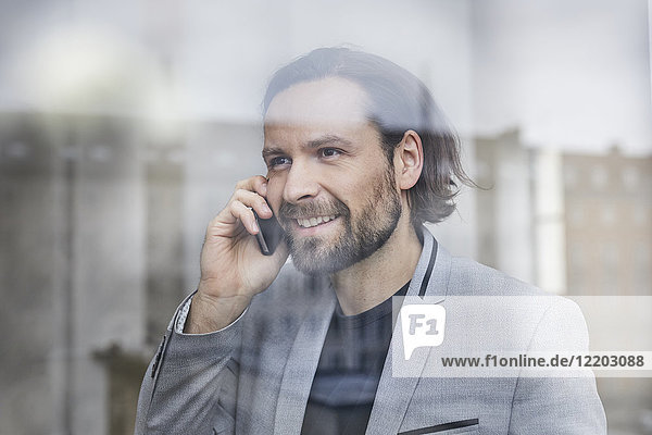 Portrait of smiling businessman on the phone behind windowpane