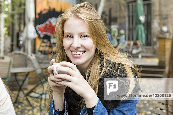 Deutschland  Berlin  Porträt einer glücklichen jungen Frau beim Kaffeetrinken im Straßencafé
