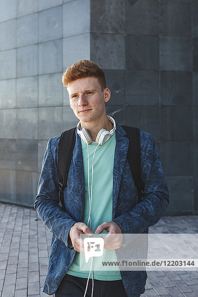 Rothaariger junger Mann im Freien mit Smartphone und Kopfhörer