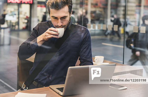 Young businessman in a cafe at train station with cup of coffee and laptop