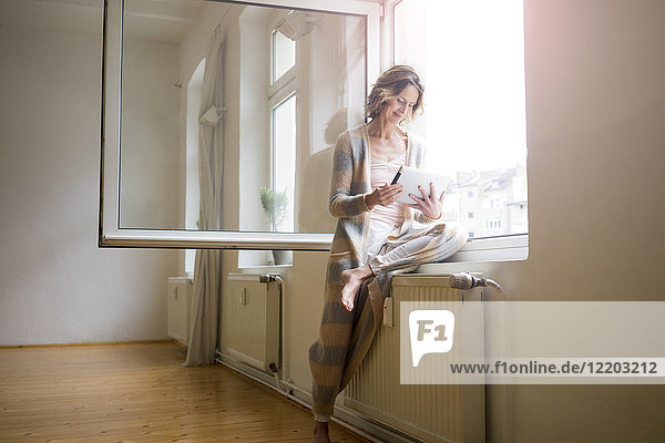 Reife Frau im leeren Raum mit Tablette am Fenster