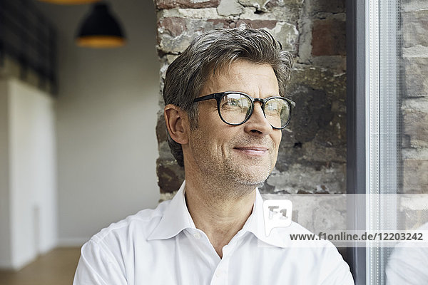 Porträt eines lächelnden Geschäftsmannes mit Brille aus dem Fenster schauend