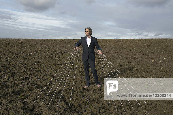 Businessman standing on a field tied to strings