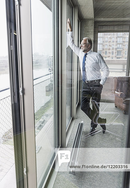 Serious mature businessman standing at the window looking out