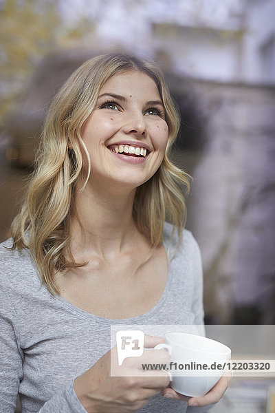 Porträt einer glücklichen Frau mit Kaffeetasse nach oben schauend
