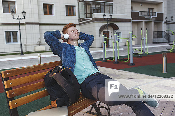 Rothaariger junger Mann mit Kopfhörer auf der Bank sitzend