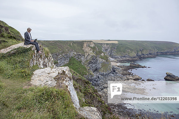 UK  Cornwall  Gwithian  businessman sitting at the coast using laptop