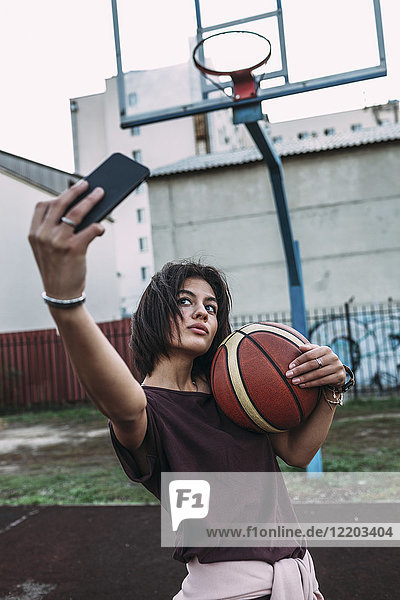 Junge Frau mit Basketball  die einen Selfie auf dem Freigelände nimmt.