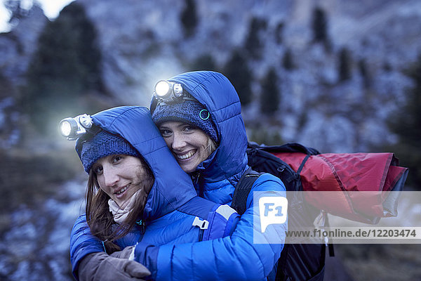 Two happy young women wearing headlamps embracing in the mountains