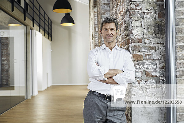 Portrait of confident businessman leaning against brick wall in modern office