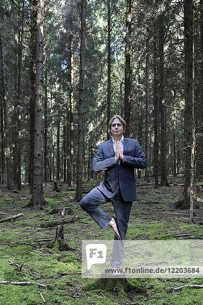 Businessman practicing yoga in forest