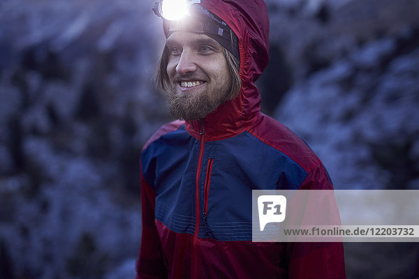 Porträt eines lächelnden Mannes mit Stirnlampe bei Dämmerung in den Bergen