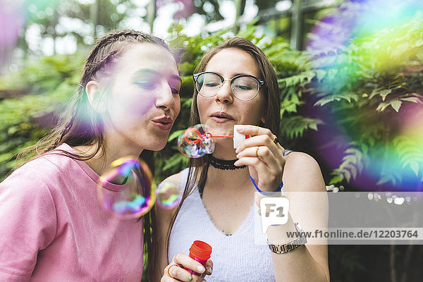 Zwei Teenager-Mädchen  die zusammen Seifenblasen blasen.