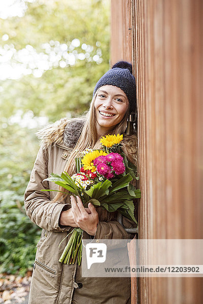 Porträt einer lächelnden jungen Frau mit Blumenstrauß im Freien