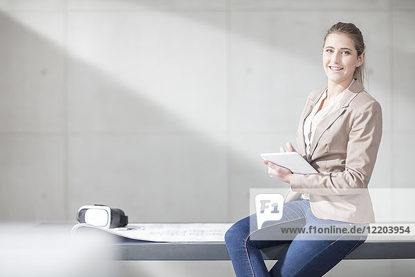 Porträt einer lächelnden jungen Frau mit Blaupause  VR-Brille und Tablette im Büro