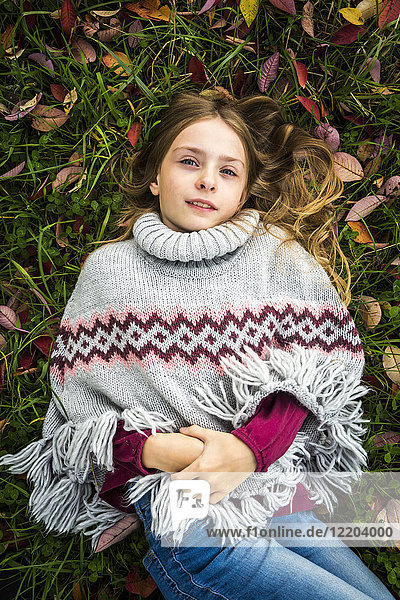 Portrait of girl wearing poncho lying on autumnal meadow