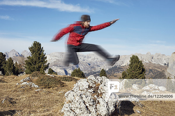Junger Mann springt über Felsen in den Bergen