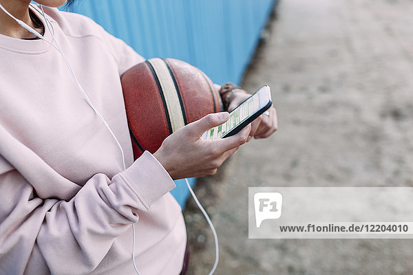 Nahaufnahme der Frau mit Basketball  Smartphone und Kopfhörer
