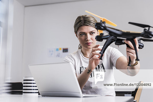 Junge Frau mit Laptop am Schreibtisch mit Drohne
