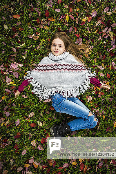 Portrait of smiling girl wearing poncho lying on autumnal meadow