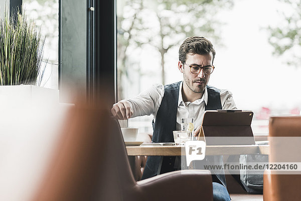Junger Mann mit Tablette am Fenster in einem Café