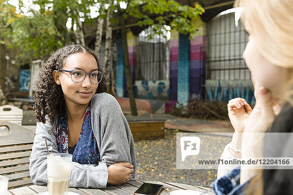 Deutschland,  Berlin,  Porträt einer jungen Frau beim Kaffeetrinken mit ihren Freunden im Straßencafé