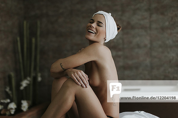 Fröhliche nackte junge Frau sitzt auf einer Liege in einem Spa