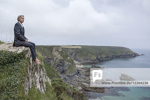UK  Cornwall  Gwithian  businessman sitting at the coast looking at view