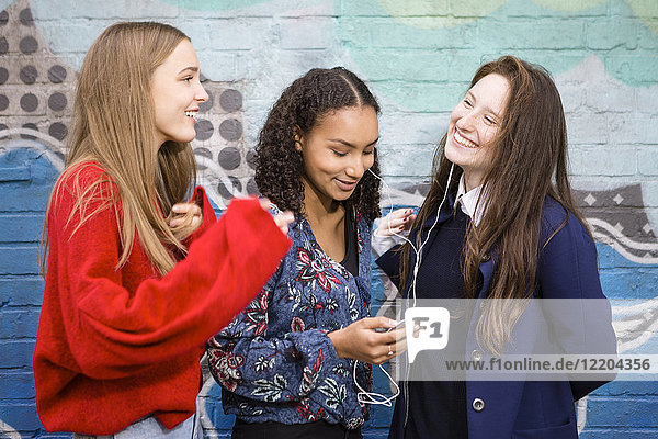 Drei Freunde stehen vor der Graffiti-Wand und hören Musik mit Smartphone und Kopfhörer.