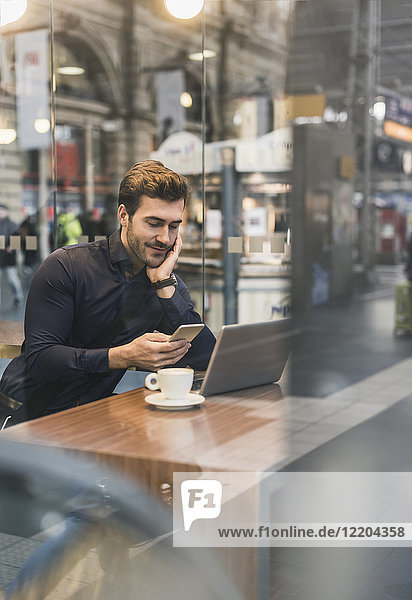 Young businessman in a cafe at train station with cell phone and laptop