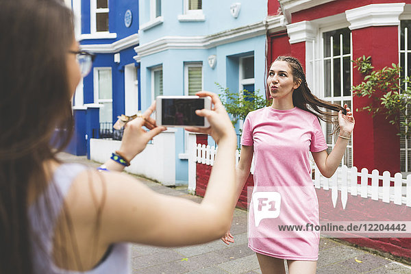 Teenage girl taking cell phone picture of young woman in the city