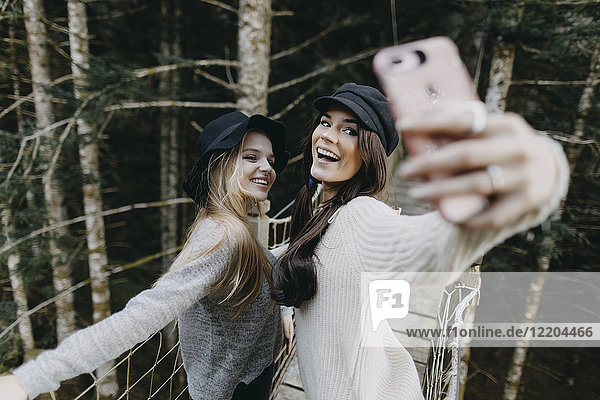 Zwei glückliche junge Frauen auf einer Hängebrücke  die einen Selfie nehmen.