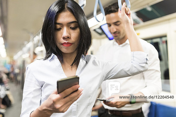 Businessman and businesswoman using cell phones in the subway