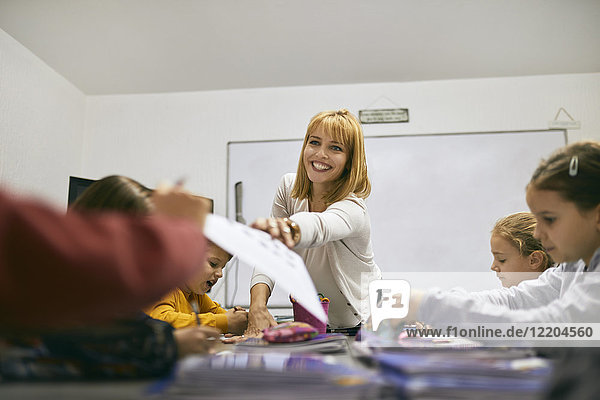 Lächelnder Lehrer überreicht dem Schüler in der Klasse ein Blatt Papier.