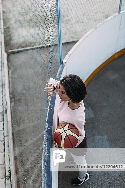 Junge Frau steht mit Basketball am Zaun