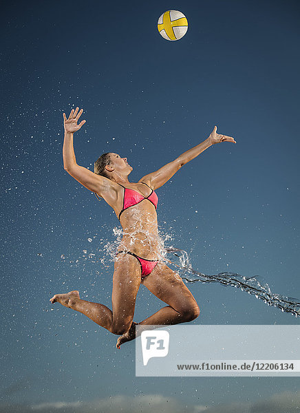 Wasser spritzt auf kaukasische Frau  die zum Volleyball springt
