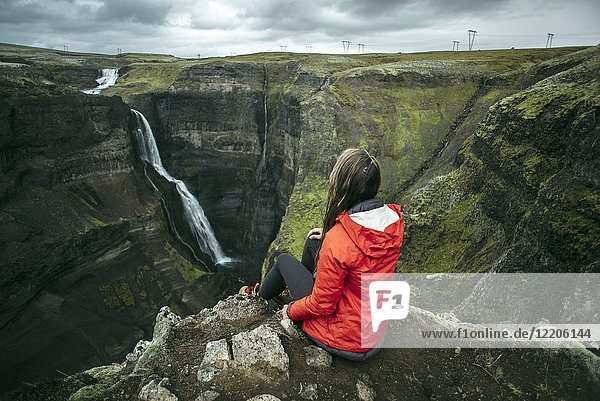 Kaukasische Frau sitzt auf einer Klippe und bewundert einen Wasserfall