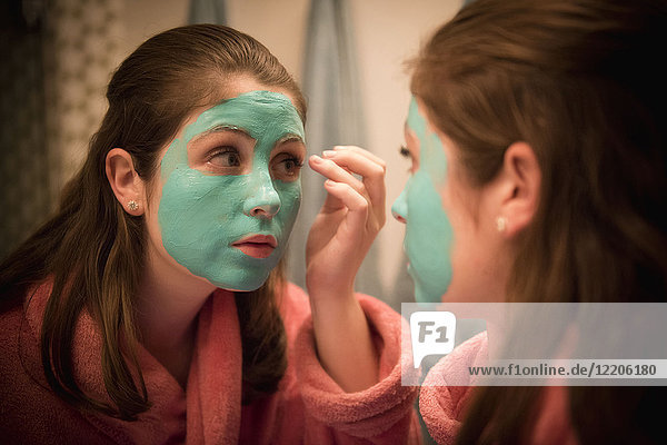 Kaukasisches Mädchen beim Auftragen einer Gesichtsmaske im Spiegel