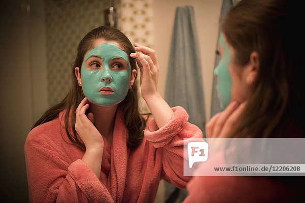 Kaukasisches Mädchen beim Auftragen einer Gesichtsmaske im Spiegel